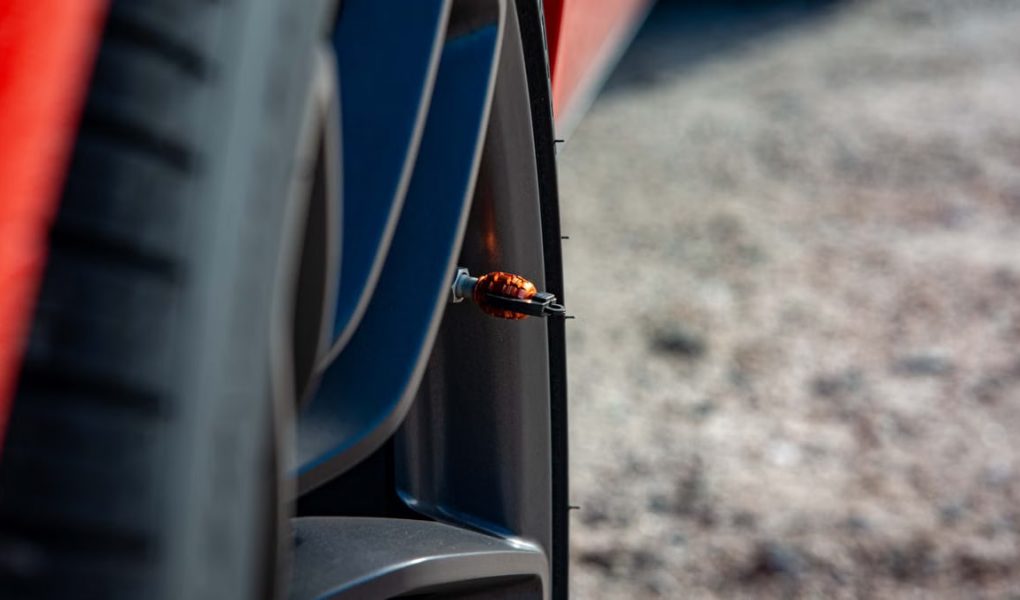 Detailed shot of a car's wheel showcasing an orange decorative tire valve cap on a sunny day.