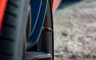 Detailed shot of a car's wheel showcasing an orange decorative tire valve cap on a sunny day.