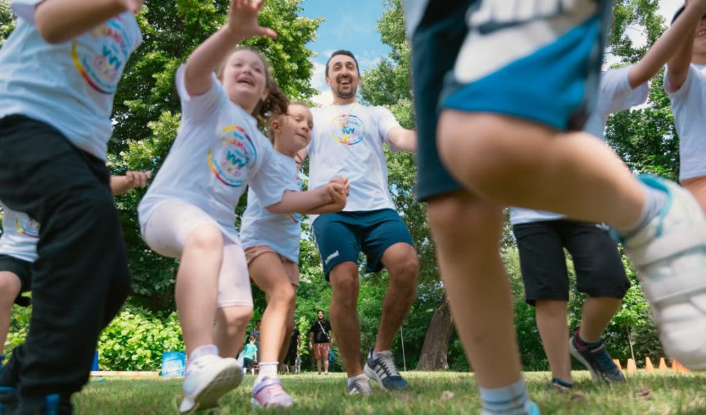 Joyful group of children and adult engaging in playful activities in a sunny park setting.