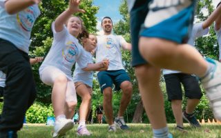 Joyful group of children and adult engaging in playful activities in a sunny park setting.