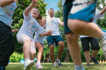 Joyful group of children and adult engaging in playful activities in a sunny park setting.